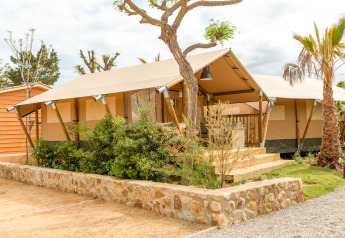 A modern safari tent at Glamping Mar with a wooden porch, lush greenery, and clear, sunny skies.
