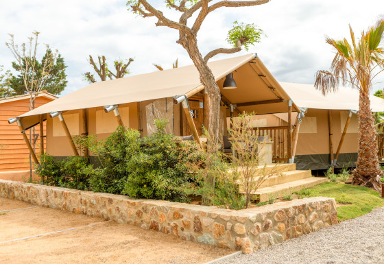 Tenda safari moderna al Glamping Mar con veranda in legno, piante verdi e un clima soleggiato e limpido.