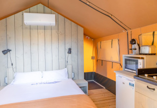 Vista interior de una tienda glamping safari en Camping del Mar, España, con cama, aire acondicionado y cocina.