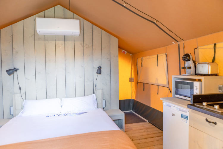 Vista interior de una tienda glamping safari en Camping del Mar, España, con cama, aire acondicionado y cocina.