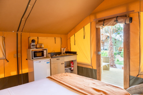 Indretning af safaritelt med tekøkken, køleskab og seng på Glamping Mar ved Camping del Mar, Spanien.