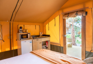 Indretning af safaritelt med tekøkken, køleskab og seng på Glamping Mar ved Camping del Mar, Spanien.