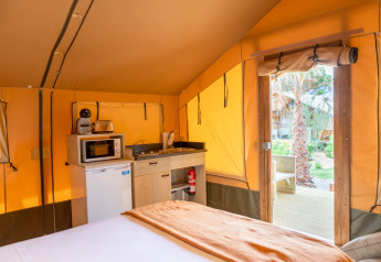 Interior de tienda safari con cocina, nevera y cama en Glamping Mar, Camping del Mar, España.