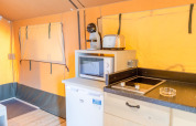 Interior of a safari tent at Glamping Mar, Camping del Mar, Spain featuring kitchen area, microwave, and fridge.