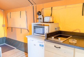 Interior of a safari tent at Glamping Mar, Camping del Mar, Spain featuring kitchen area, microwave, and fridge.