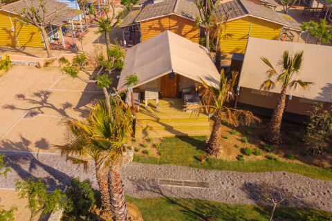 Vista aérea de la tienda safari Glamping Mar en Camping del Mar, España, rodeada de palmeras y jardines verdes.