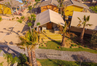 Luftfoto af en safari telt Glamping Mar ved Camping del Mar i Spanien, omgivet af palmer og grønne områder.