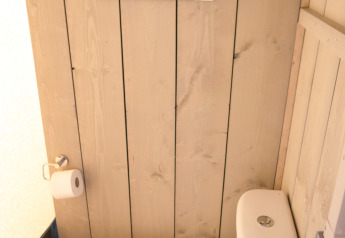 Un inodoro moderno en un baño con paredes de madera y espejo, en una tienda safari de Glamping Mar, España.