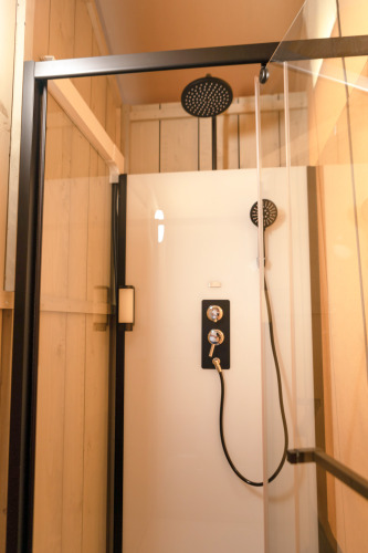 Ducha moderna con puerta de cristal y grifería negra en una tienda safari de Glamping Mar en Camping del Mar, España.