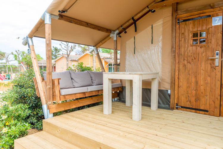 Terraza exterior de una tienda safari en Glamping Mar, Camping del Mar, España, con banco y mesa.