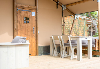 Veranda in legno con tavolo e sedie davanti a tenda safari al Glamping Mar, Camping del Mar, Spagna.