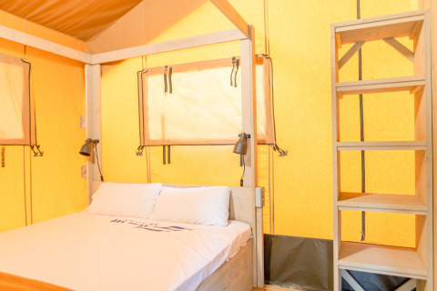 Vista interior de una tienda safari con cama y estantería en Glamping Mar en Camping del Mar en España.