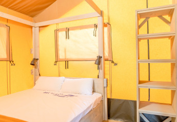 Interior view of a safari tent with bed and shelving at Glamping Mar at Camping del Mar in Spain.