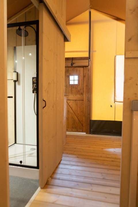 Interieur van een safaritent met houten vloer, douchecabine en houten deur bij Glamping Mar, Camping del Mar, Spanje.