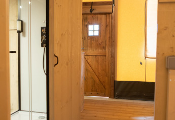 Interior de tienda safari con suelo de madera, cabina de ducha y puerta de madera en Glamping Mar, Camping del Mar, España.