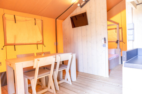 Interiør af en safariteltsuite på Glamping Mar, Camping del Mar, med spisebord, tv og soverum.