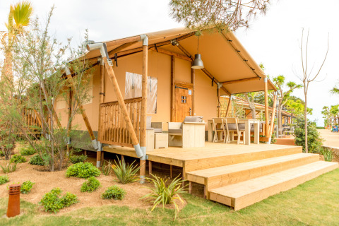 Safari-tent Glamping Mar met houten terras en tuinmeubilair bij Camping del Mar in Spanje, omringd door planten.