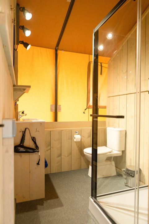 Baño en una tienda safari de Glamping Mar en Camping del Mar, España, con ducha y retrete modernos.