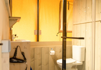 Baño en una tienda safari de Glamping Mar en Camping del Mar, España, con ducha y retrete modernos.