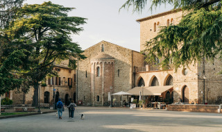 Ein ruhiger Platz in Bevagna, Umbrien, Italien, umgeben von alten Steingebäuden, Bäumen und Spaziergängern.
