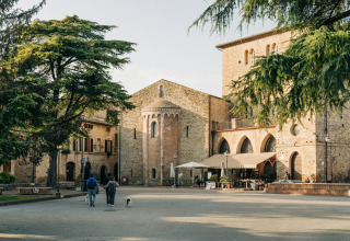 Et fredeligt torv i Bevagna, Umbrien, Italien, med gamle stenhuse, træer og folk der går med deres hunde.