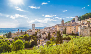 Vista panorámica de Bevagna, Umbría, Italia, con edificios históricos y colinas verdes bajo un cielo soleado.