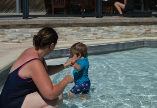 Een vrouw begeleidt een klein kind in een ondiep zwembad bij Camping Seasonova Haliotis in Normandië, Frankrijk.