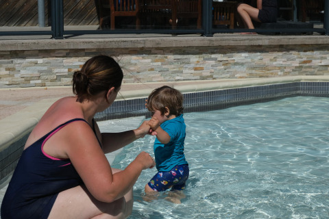 Una mujer ayuda a un niño pequeño en una piscina poco profunda en Camping Seasonova Haliotis, Normandía, Francia.