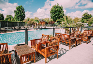 Area piscina all'aperto con sedute in legno e palme al Camping Seasonova Haliotis, parco vacanze in Normandia, Francia.