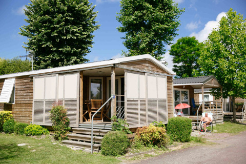 Wooden cabin at Camping Seasonova Haliotis holiday park in Normandy, France, with porch and green surroundings.