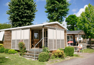 Wooden cabin at Camping Seasonova Haliotis holiday park in Normandy, France, with porch and green surroundings.
