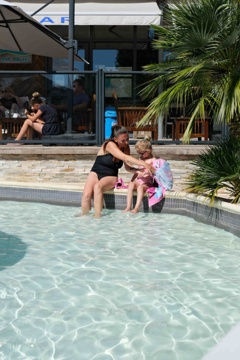 Madre e hija sentadas junto a la piscina en Camping Seasonova Haliotis, un parque vacacional en Normandía, Francia.