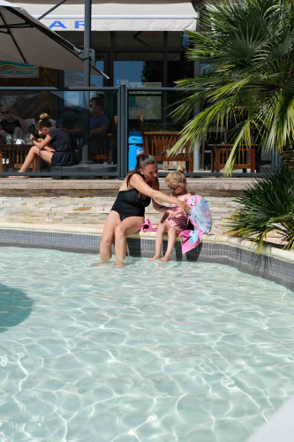 Mother and child sit by the pool at Camping Seasonova Haliotis holiday park in Normandy, France.