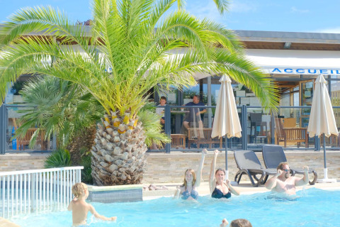 Bezoekers ontspannen in het zwembad met palmbomen bij Camping Seasonova Haliotis in Normandië, Frankrijk.