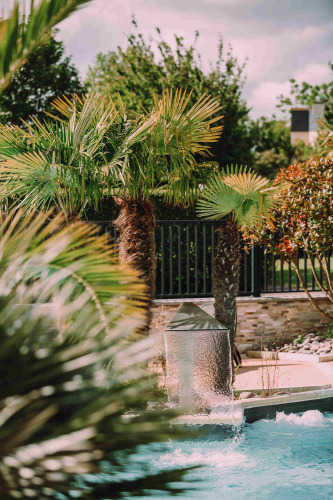 Swimming pool with fountain surrounded by palm trees at Camping Seasonova Haliotis in Normandy, France.