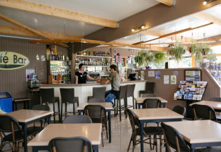 Innenansicht der Cafébar im Camping Seasonova Haliotis mit Tischen, Stühlen und hängenden Pflanzen.