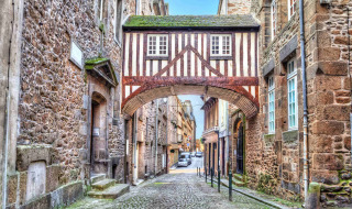 Casa entramada sobre una calle adoquinada en Pontorson, Normandía, Francia, rodeada de edificios antiguos.