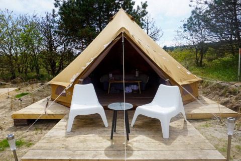 Un tipi Bell Escape Family con dos sillas blancas y una mesa pequeña afuera, rodeado de naturaleza.