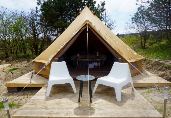 Un tipi Bell Escape Family con dos sillas blancas y una mesa pequeña afuera, rodeado de naturaleza.