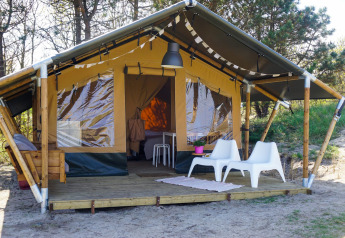 Tenda safari Lodge Escape con terrazza in legno, due sedie bianche e scenario naturale.