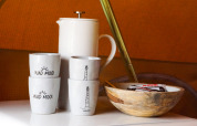 Tazas de cerámica, jarra blanca y cuenco de madera sobre una mesa en alojamiento glamping acogedor.