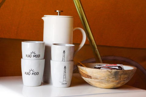 Tazas de cerámica, jarra blanca y cuenco de madera sobre una mesa en alojamiento glamping acogedor.