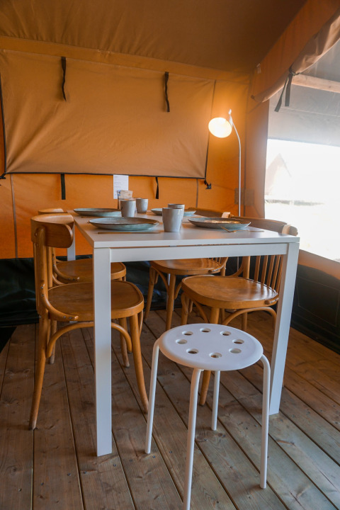 Indendørs spisebord med fire træstole og en hvid skammel i Lodge Escape safari-telt, Holland.