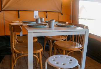 Tavolo da pranzo interno con quattro sedie in legno e sgabello bianco nella tenda Lodge Escape, Olanda.