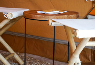 Innen im Bell Escape Tipi-Zelt bei Little Canvas Escape, Niederlande, mit Bambusstühlen und Holztisch.