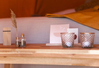 Dichtbij een houten tafel met kleine glazen vaasjes, kaarten en kaarsen in de Bell Escape tent.