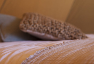 Primer plano de una cama con manta beige y cojín dentro de una tienda tipi iluminada con luz cálida.