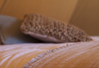 Nærbillede af en seng med beige tæppe og pude inde i et tipitelt, med dæmpet og varm belysning.