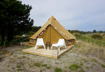 Et billede af et Bell Escape Family tipitelt ved Little Canvas Escape i Holland med to hvide stole foran.