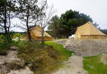 To tipi-telte ved Little Canvas Escape i Holland, omgivet af træer, sand og grønne områder.